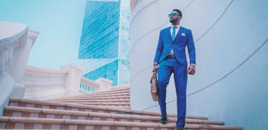 A man in a tailored blue suit, walking down a set of stairs on an outdoor building.