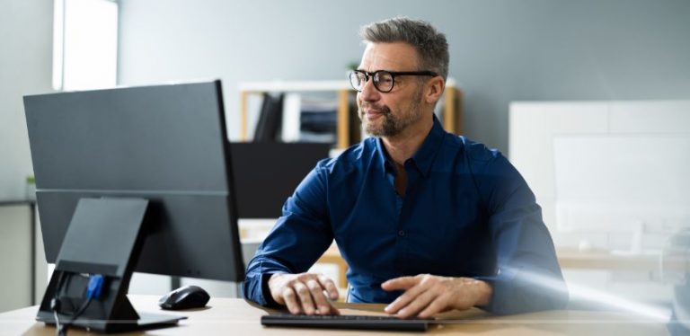 An older man sitting at a desk using a desktop computer.