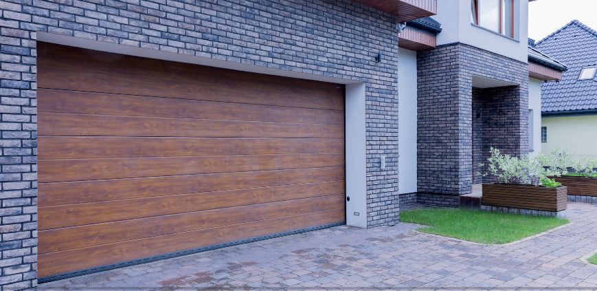 A black brick house with a new, dark brown garage door.