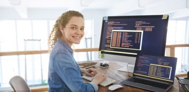 A woman sitting at a desk in front of two computer screens.