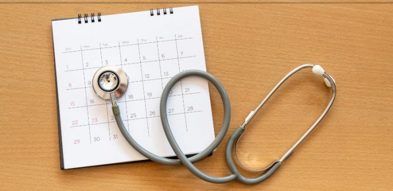 A stethoscope laying on top of a paper calendar, on a brown table.