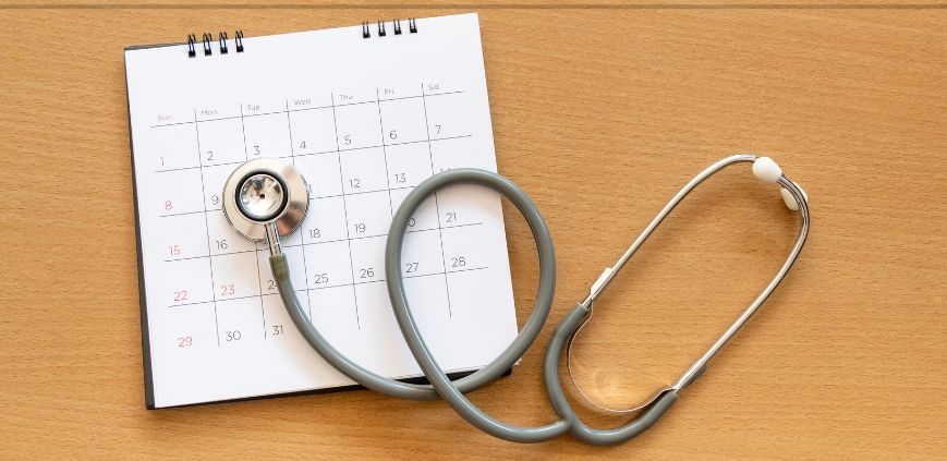 A stethoscope laying on top of a paper calendar, on a brown table.