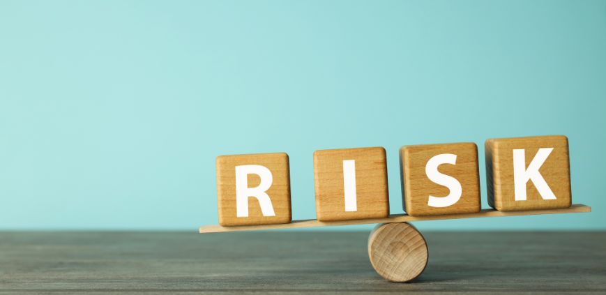 Wooden blocks that spell RISK balancing on a wooden dowel against a blue background.