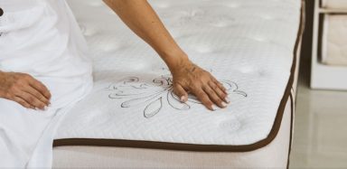 A woman sitting on a mattress, pushing down her hand to see how comfortable it is.