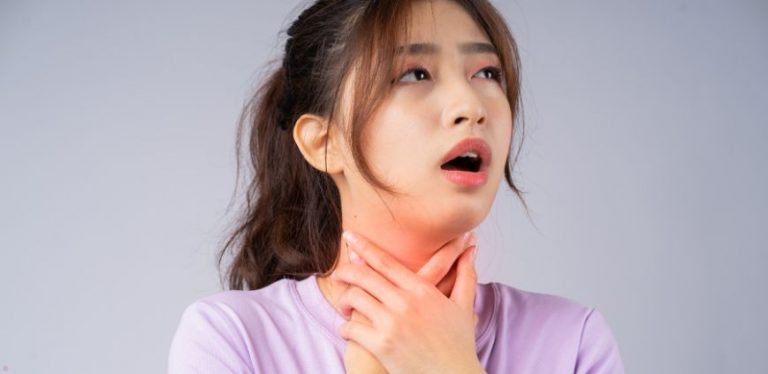 A woman in a purple shirt holding her throat, as if experiencing throat inflammation.