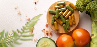 Supplements on a brown dish, beside various vegetables.